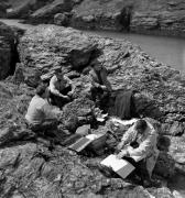 Marcel Carné, Alexandre Trauner (de dos) et son équipe lors d'un pique-nique de travail sur les rochers de la côte sauvage dans "La Fleur de l'âge" de M. Carné et J. Prévert, Belle-Ile, 1947